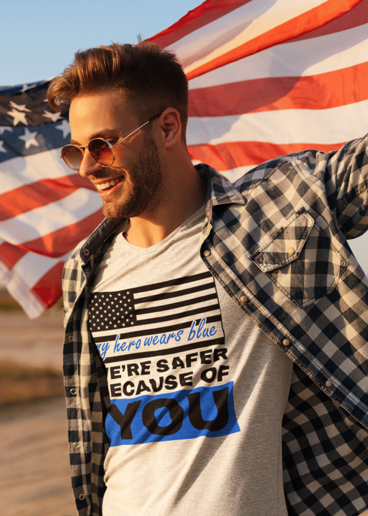 Stylish man outdoors holding an American flag, wearing a Hero Hues t-shirt with blue lives matter style message.